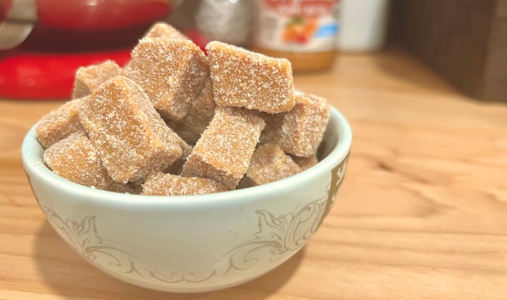 Easy Keto Peanut Butter fudge is so simple to make and so delicious. This image is of a cute little ceramic bowl, filled over the top with chunks of delicious peanut butter fudge, sitting on a warm wood countertop, with kitchen appliances in the background.