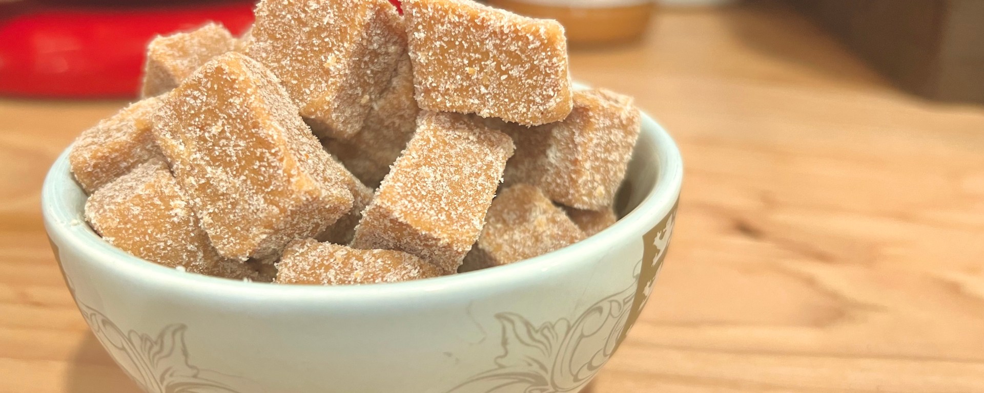 Easy Keto Peanut Butter fudge is so simple to make and so delicious. This image is of a cute little ceramic bowl, filled over the top with chunks of delicious peanut butter fudge, sitting on a warm wood countertop, with kitchen appliances in the background.
